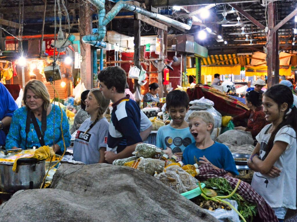 Tourists and local vendors at a night food market in Siem Reap with fresh produce and lit stalls