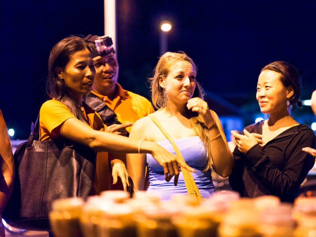 Akim Ly pointing out local dishes to two guests at a Siem Reap night market during the After Dark Food Tour