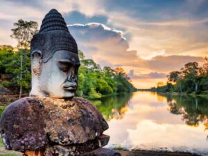Giant stone Asura head from the causeway outside Angkor Thom south gate at sunset, moat reflecting the golden sky
