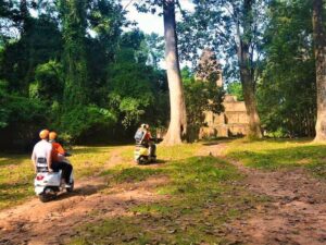 Twee gasten op oranje en witte Vespa's pauzeren op een bospad voor een kleine bakstenen Angkor-toren