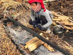 Local Khmer woman in a red headscarf tending a bamboo-rice (kralan) fire in the Siem Reap countryside
