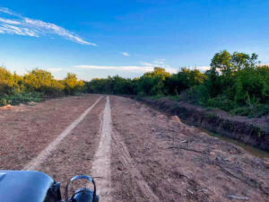 Aerial view of a line of vintage military jeeps parked on a red dirt track beside green fields during a countryside tour