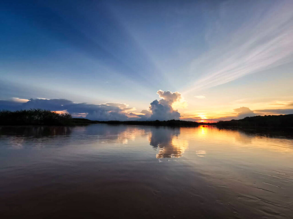 Zonsondergang boven rustige rivier met beboste oevers en gouden licht weerspiegeld op het water