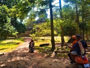 Vespa-rijders die een bospad met bomen volgen richting een oude tempel in het archeologisch park van Angkor