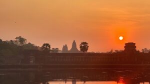 Angkor Wat silhouette under an orange sunrise with the sun rising beside the northern tower, reflected in the moat