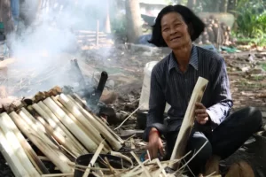 Smiling Khmer woman tending a smoking bamboo-rice (kralan) fire in the Siem Reap countryside