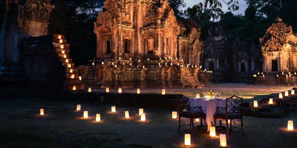 Private candlelit dinner for two set up in front of a softly lit Angkor temple at night