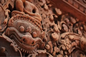 Close-up of a pink sandstone lion-face carving at Banteay Srei, surrounded by intricate floral bas-reliefs