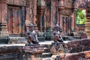 Row of kneeling guardian statues in front of the pink sandstone shrines at Banteay Srei temple