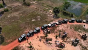 Aerial view of a line of vintage military jeeps and an oxcart parked along a red dirt road in the Siem Reap countryside