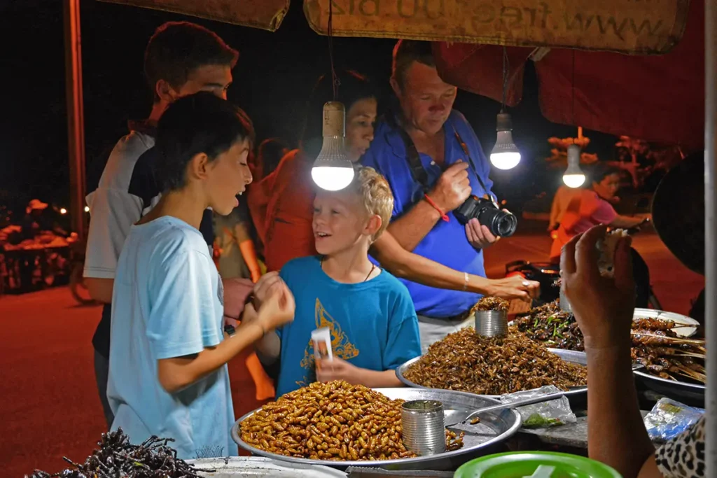 Family and children sampling insects and street food at a Siem Reap night market stall