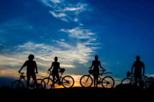Four cyclists silhouetted with their bikes against a deep blue and orange sky at sunset