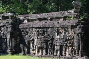 Carved stone wall at Terrace of the Elephants with detailed relief figures of elephants and attendants, surrounded by jungle foliage