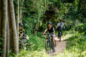 Stuurzicht van een elektrische mountainbike op een rood aarden pad naast een irrigatiesloot in het platteland van Angkor bij zonsondergang