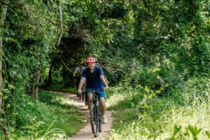 Cyclist riding through lush forest canopy on a shaded path near Angkor moat