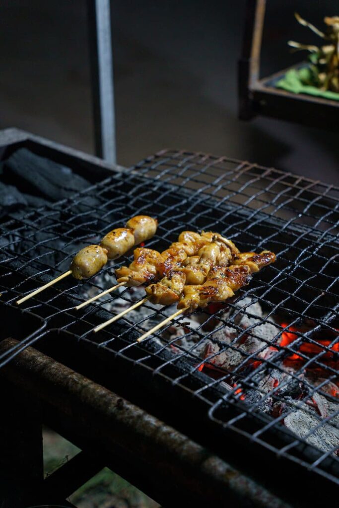 Four skewers grilling on a barbecue during a Siem Reap food tour in Cambodia
