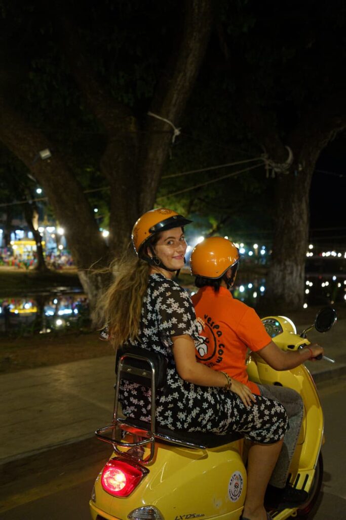Female guest riding pillion behind a female driver on a Vespa during a Siem Reap night food tour