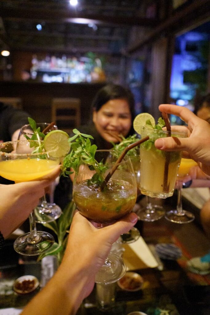Cocktail glasses raised for a toast during a Siem Reap food tour, with a smiling face in the background