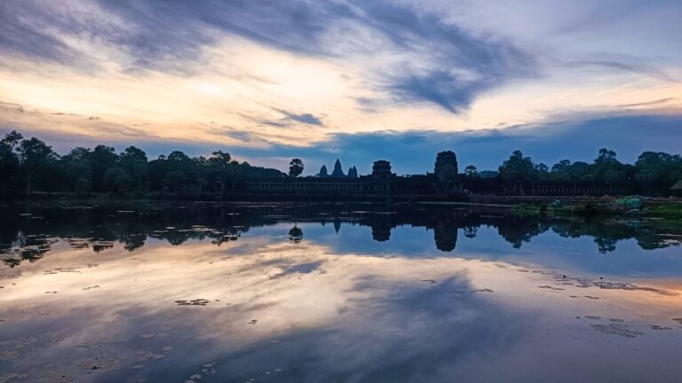 Les cinq tours d'Angkor Vat se reflétant dans l'eau calme à l'aube sous un ciel nuageux