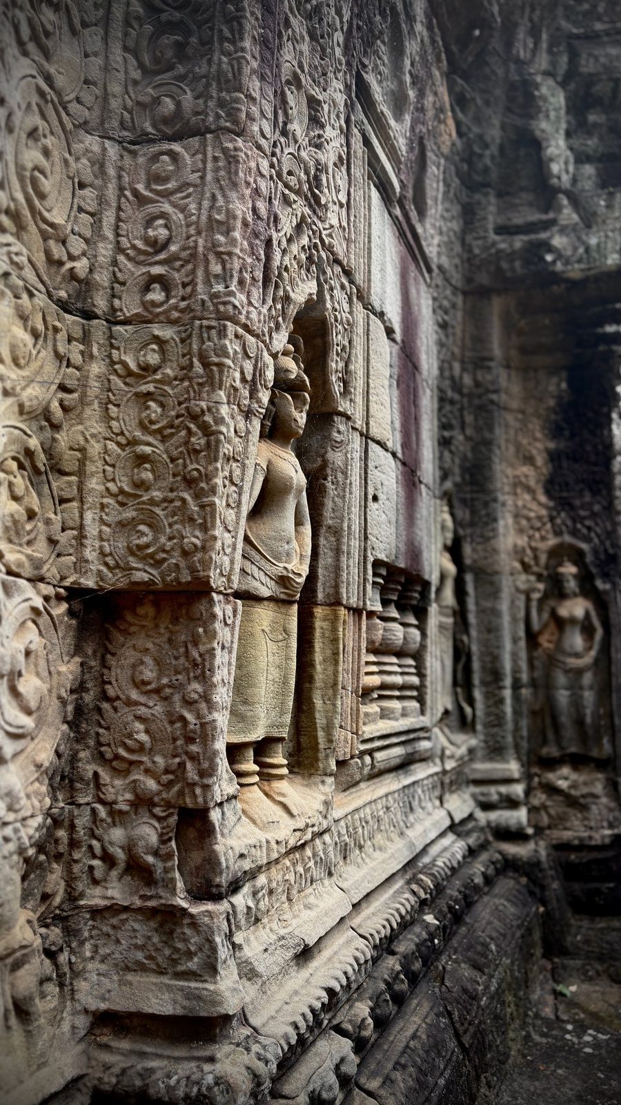A carved devata figure beside a carved stone window at Angkor Wat