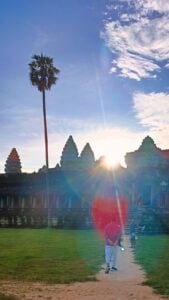 Visitor photographs Angkor Wat at sunrise framed by a palm tree.