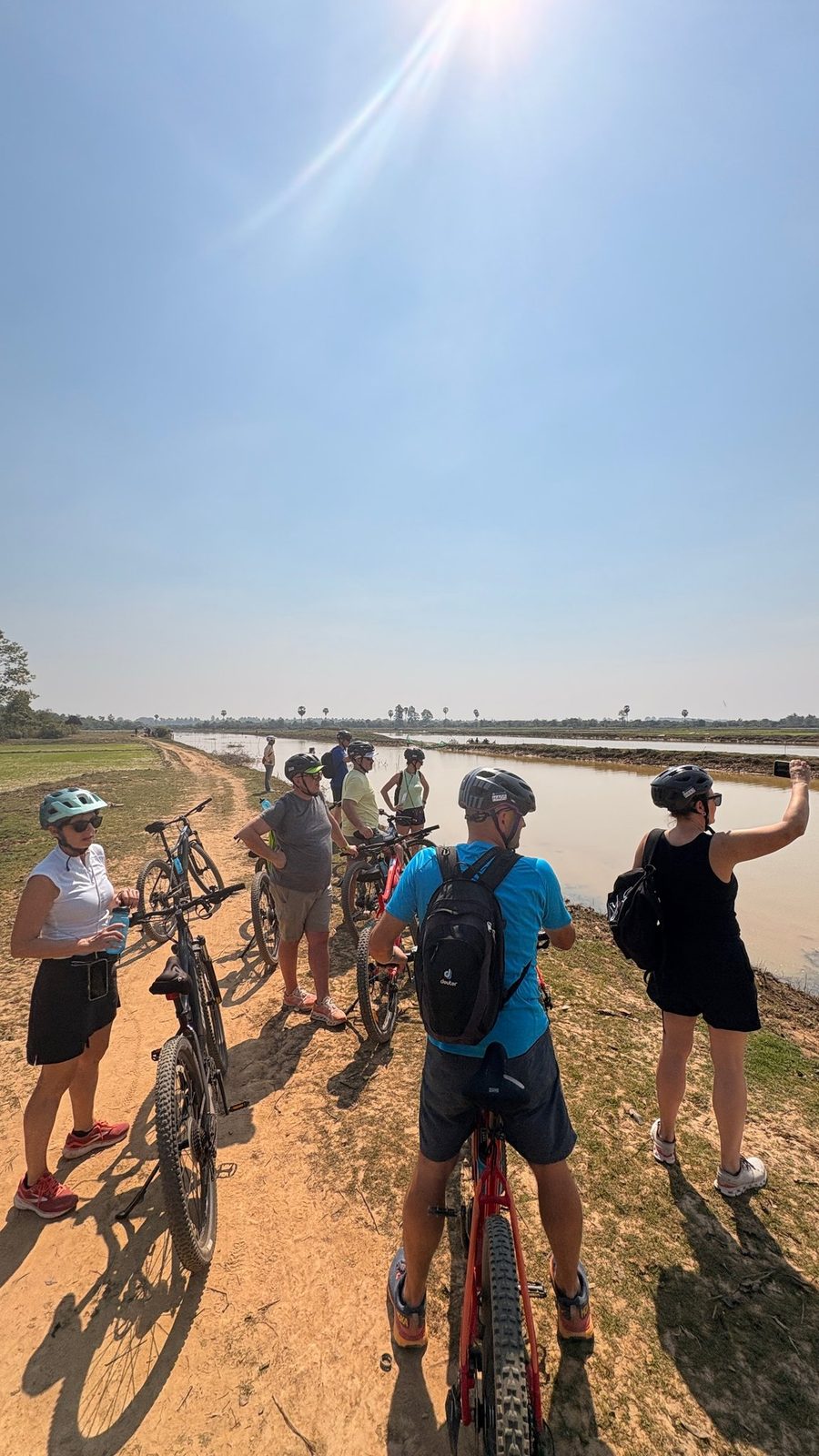 A cycling group resting on a dirt path beside Cambodian rice fields near Siem Reap