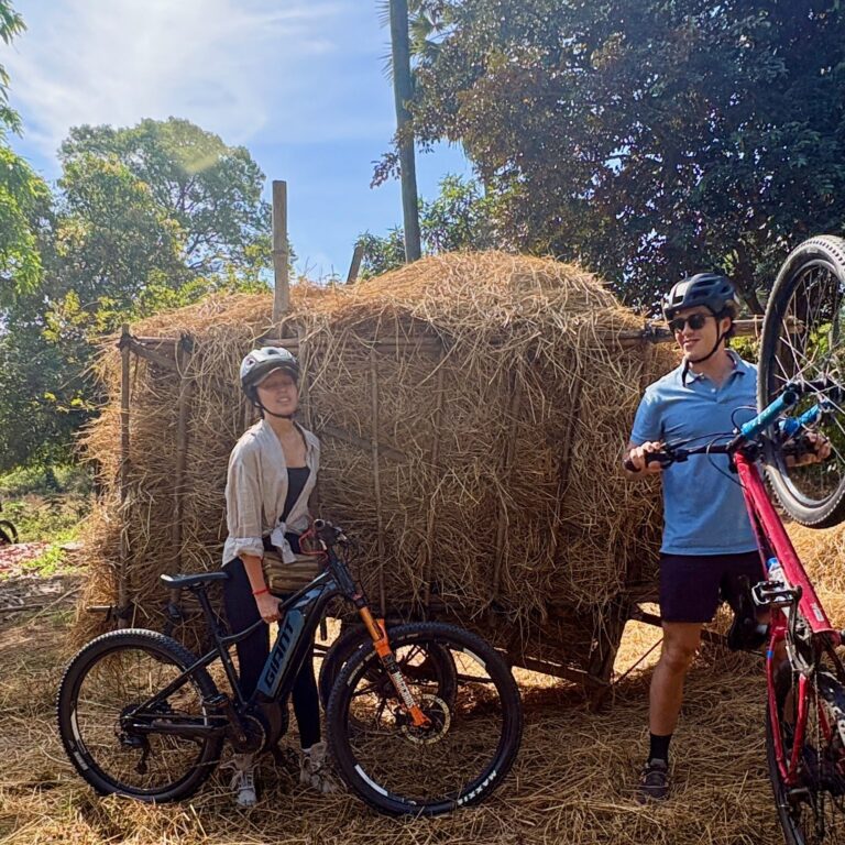 Two cyclists resting beside a straw shelter in rural Cambodia