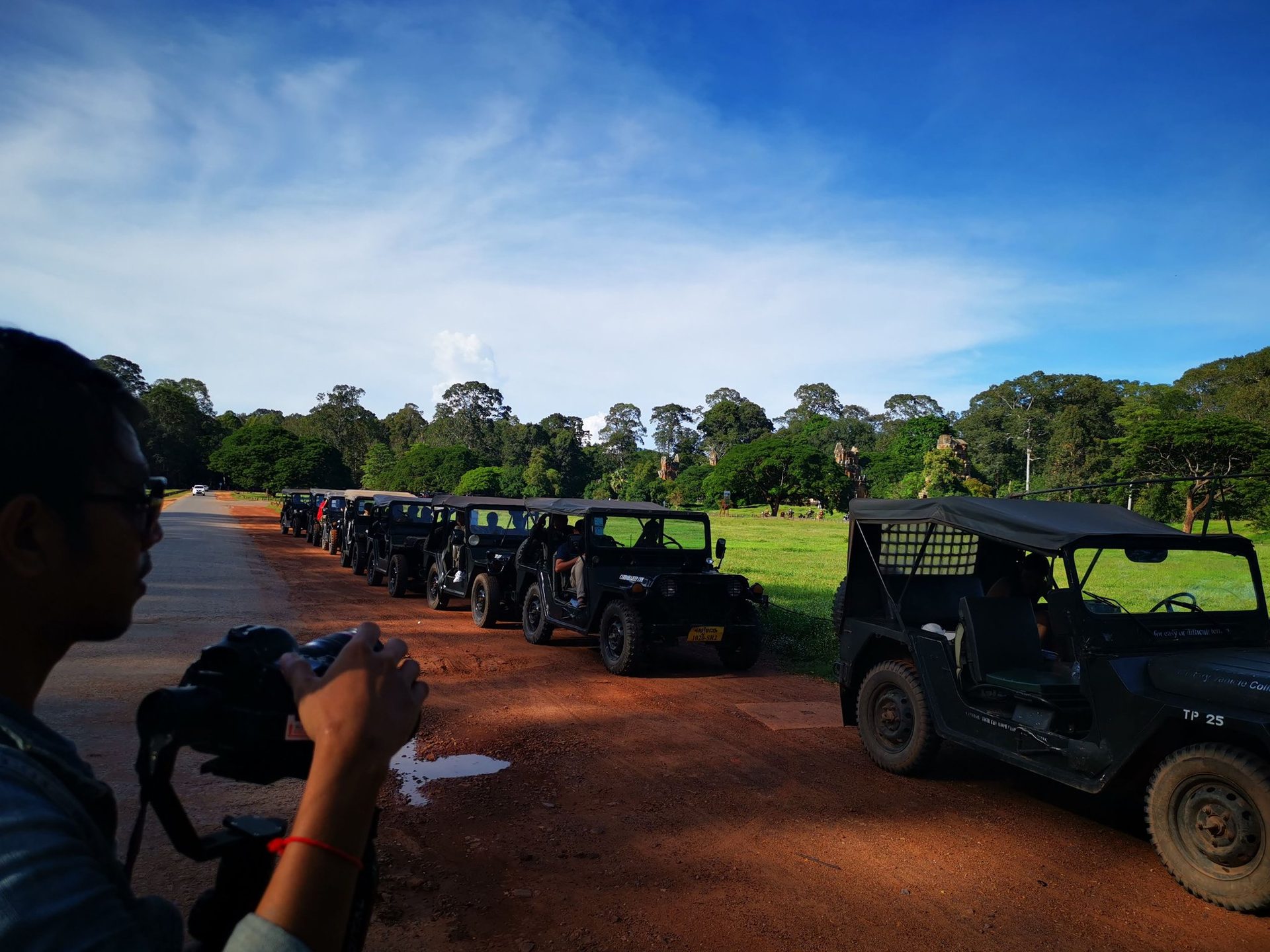 Ligne de jeeps Willys vintage garées sur une route de terre rouge à Angkor.