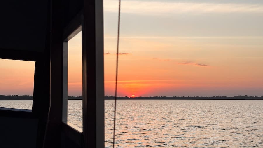 Sunset over the Tonlé Sap seen from inside a wooden boat, orange sky reflected on calm water