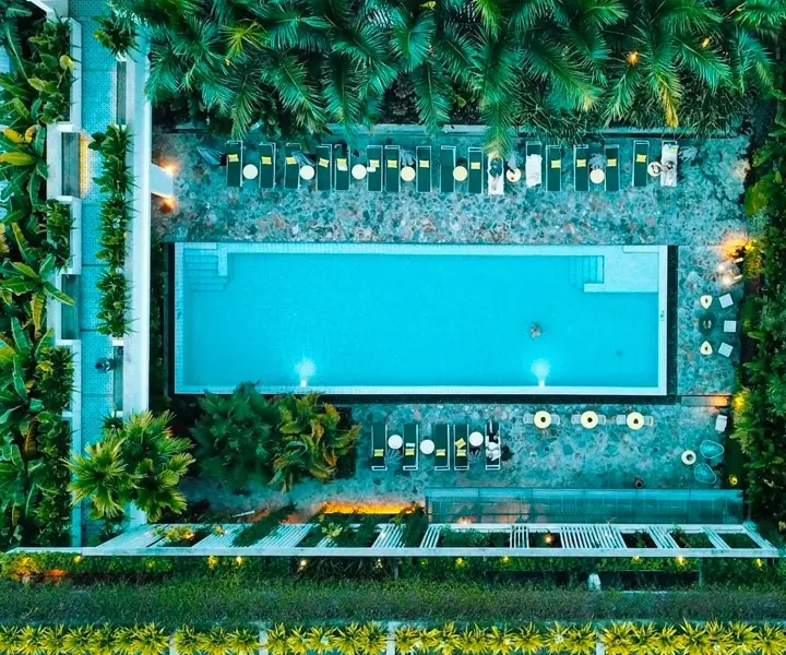 Overhead view of Viroth's Hotel pool at dusk between palm trees and rows of loungers in Siem Reap