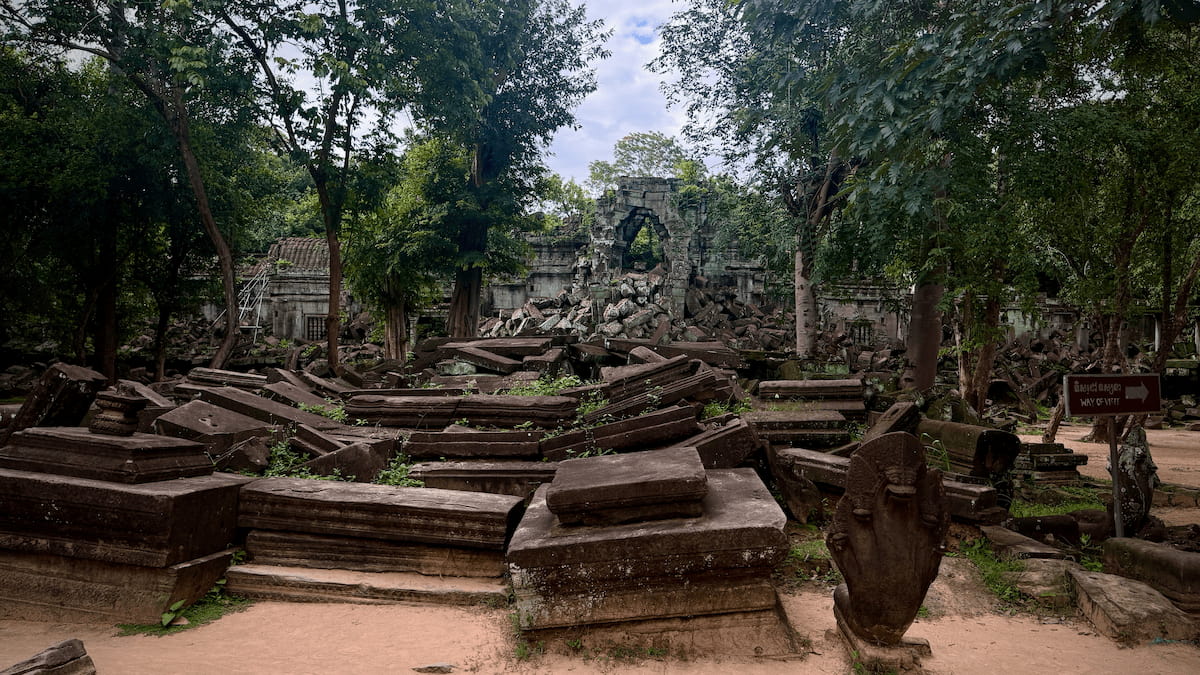Rows of fallen sandstone blocks and a carved naga head beside the visitor path at Beng Mealea