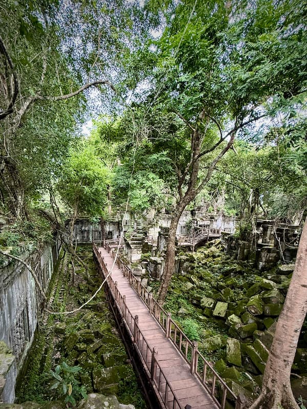 The raised wooden walkway running above the moss-covered collapsed galleries at Beng Mealea temple