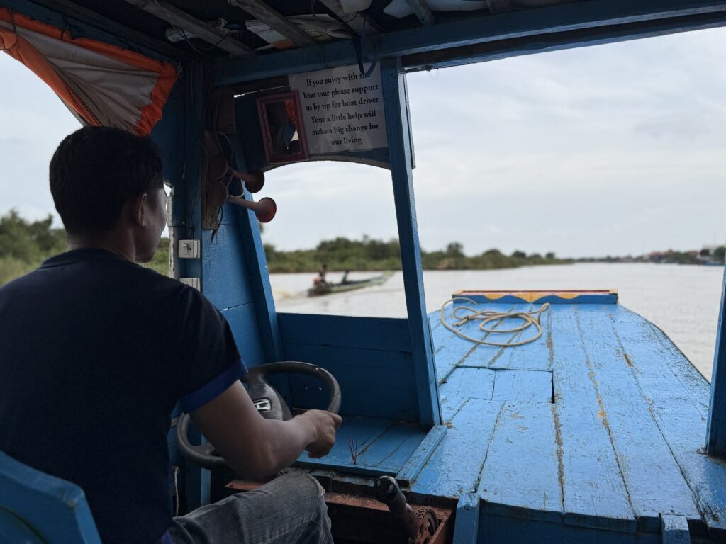 The boat driver at the wheel of a covered wooden boat on the Kampong Phluk channel