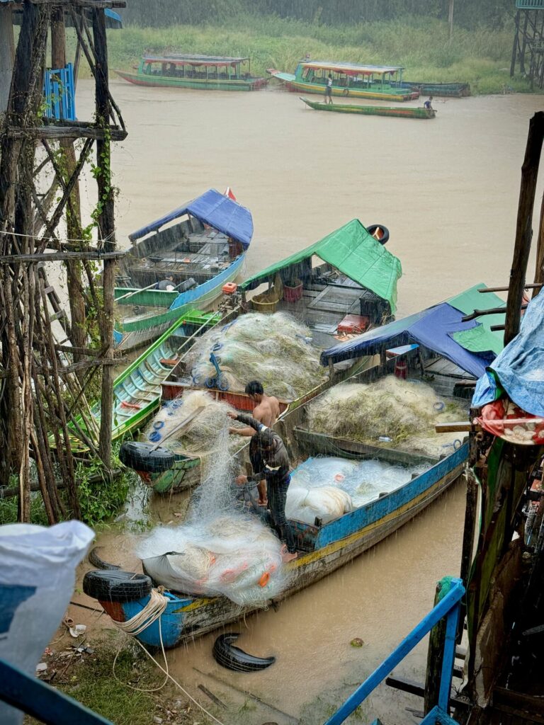 Fishermen handling nets on loaded boats at the Kampong Phluk landing in the rain