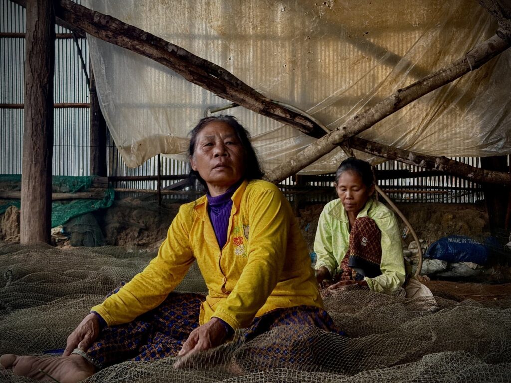 Women of Kampong Phluk seated on a pile of fishing nets, repairing them by hand