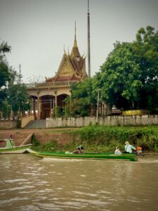 The Kampong Phluk pagoda seen from the water with a green longtail boat passing