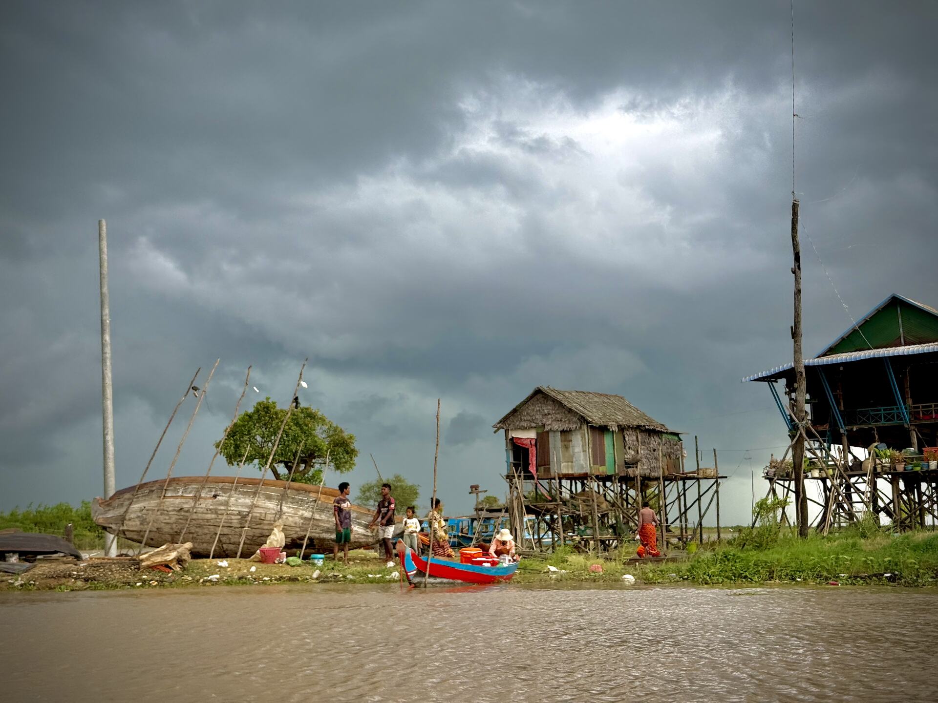 Wooden boats pulled up on the Kampong Phluk shoreline under heavy monsoon clouds