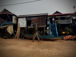 A man pulls a wooden boat along the village street in front of Kampong Phluk stilt houses