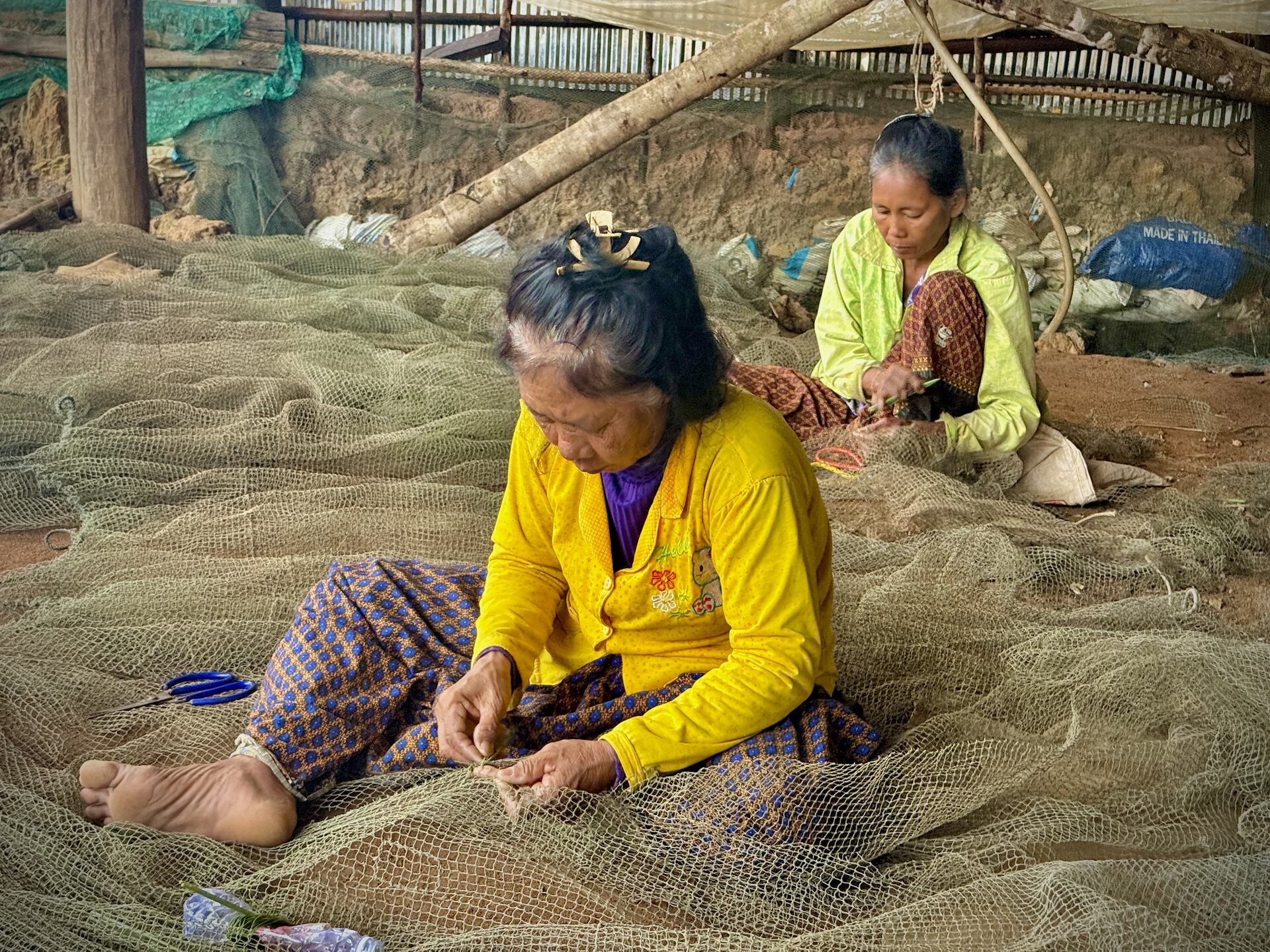 Two women mending fishing nets under a shelter in Kampong Phluk