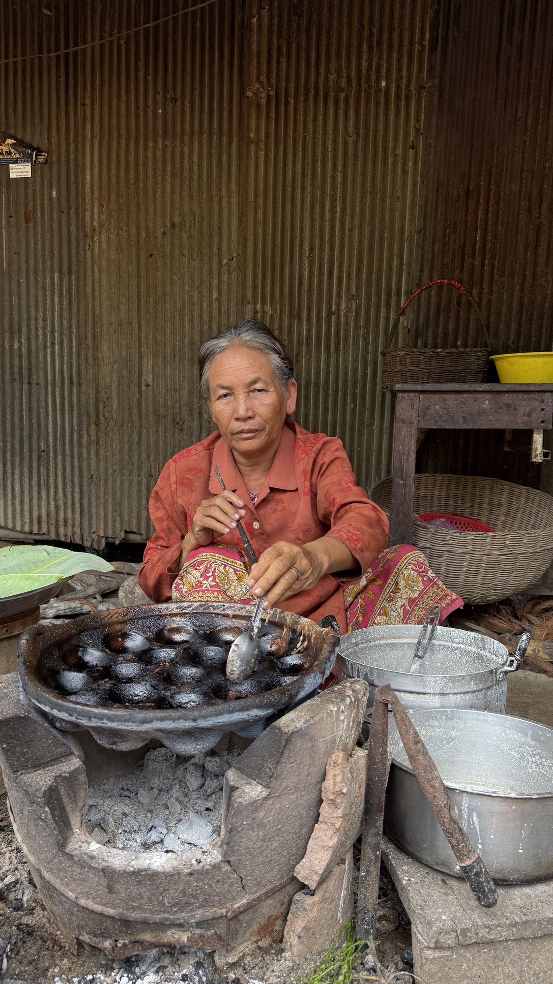 The cake maker lifts Nom Krok from the pan with a long spoon at her roadside stove