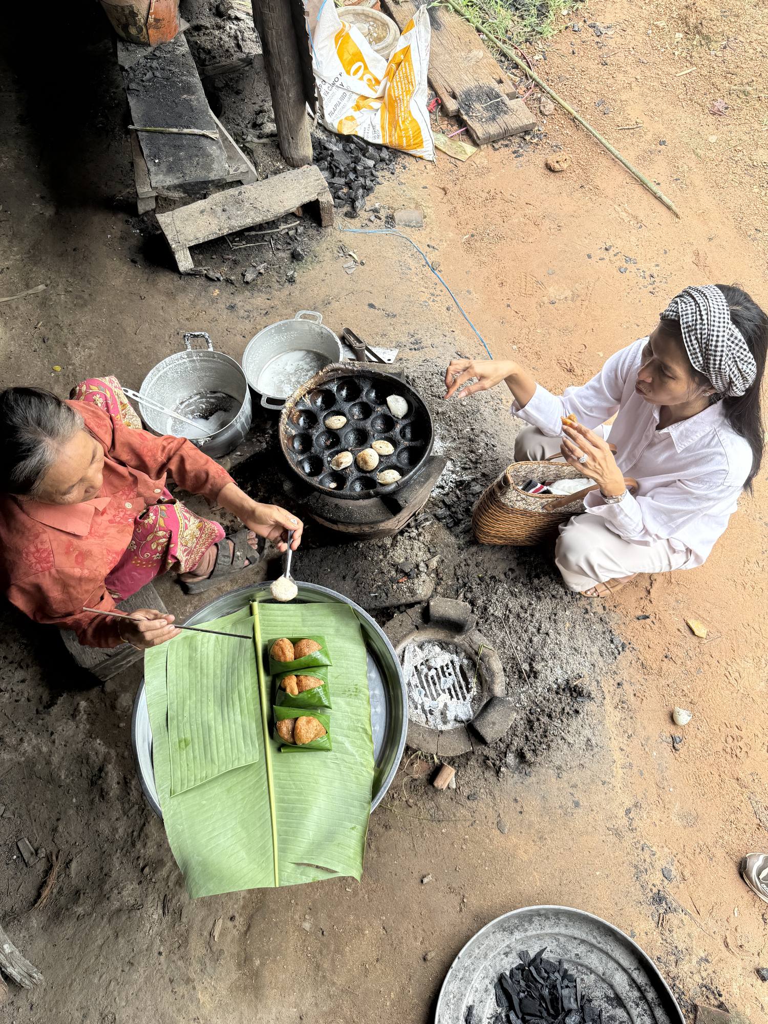 A guest sits beside the cake maker as Nom Krok cook in a cast-iron dimpled pan over charcoal