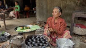 Nom Krok cooking in their pan next to finished cakes wrapped on a banana leaf